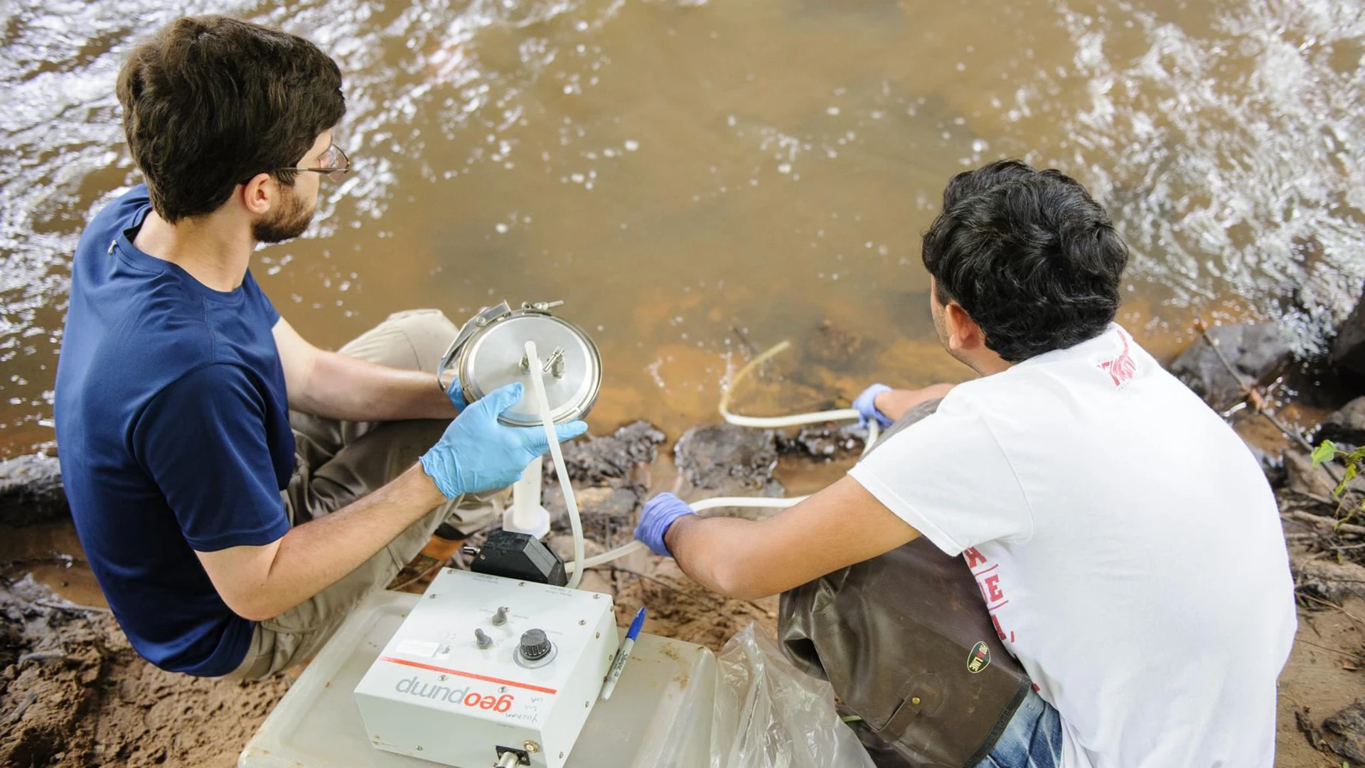 Two men use water testing equipment on a body of water in Alabama.